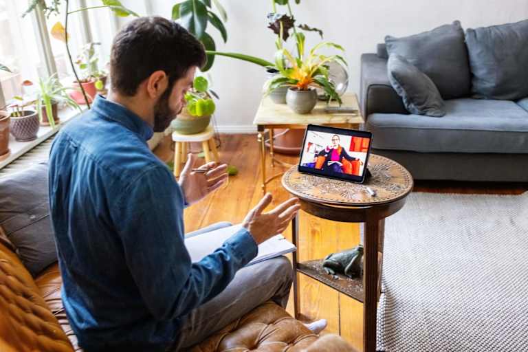Male patient having an online therapy session with his psychotherapist. The therapist is seen listening and taking notes on screen on the patient's digital tablet.