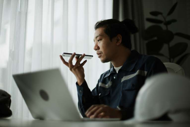 Man working on laptop while speaking into smartphone