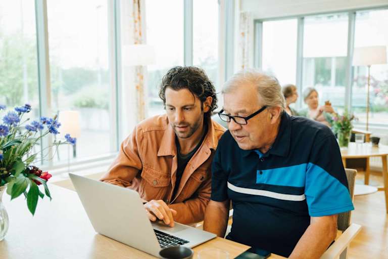 Social worker helping senior citizen with laptop
